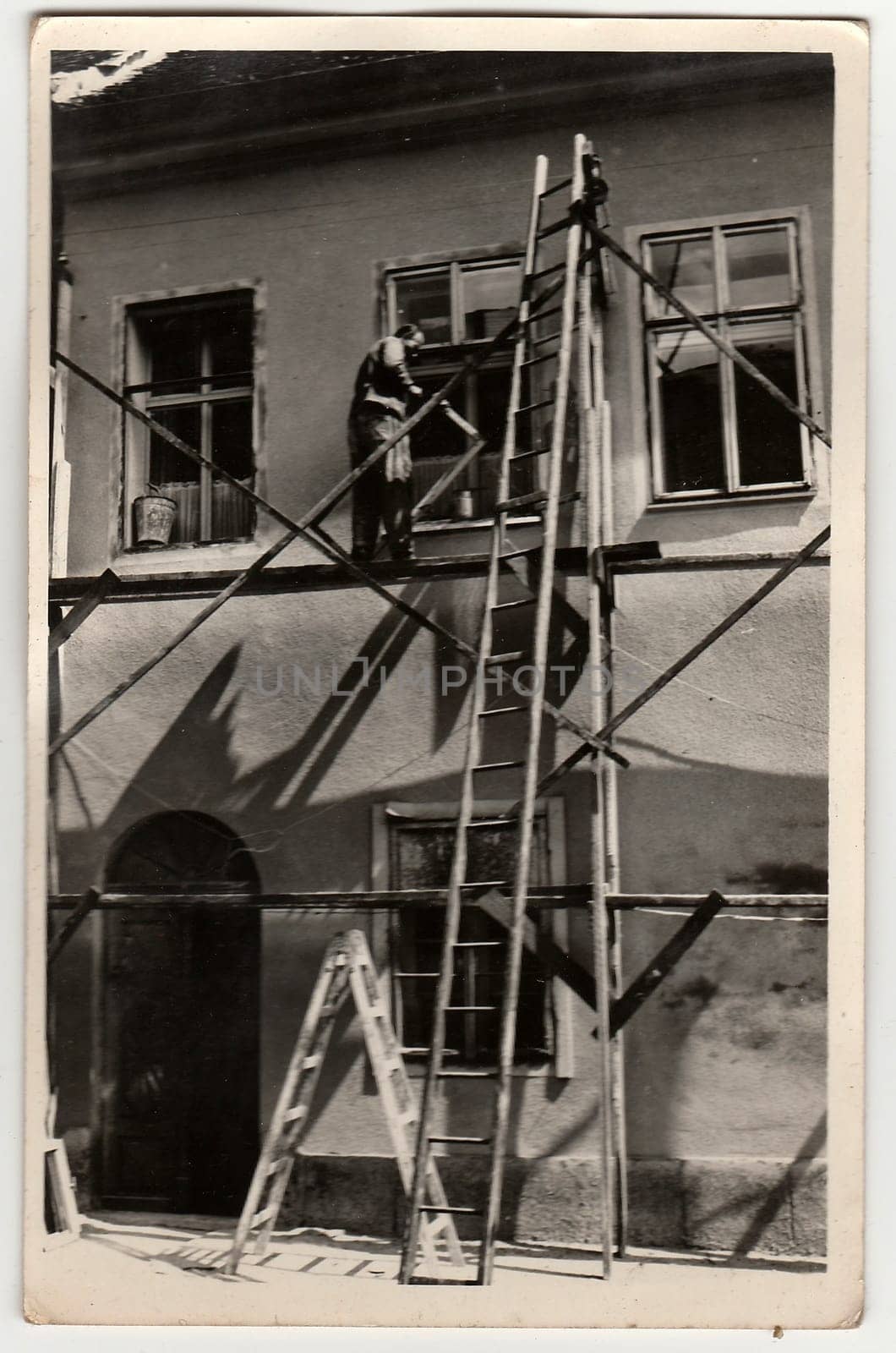 Vintage photo shows bricklayer works on wooden scaffolding. by roman_nerud