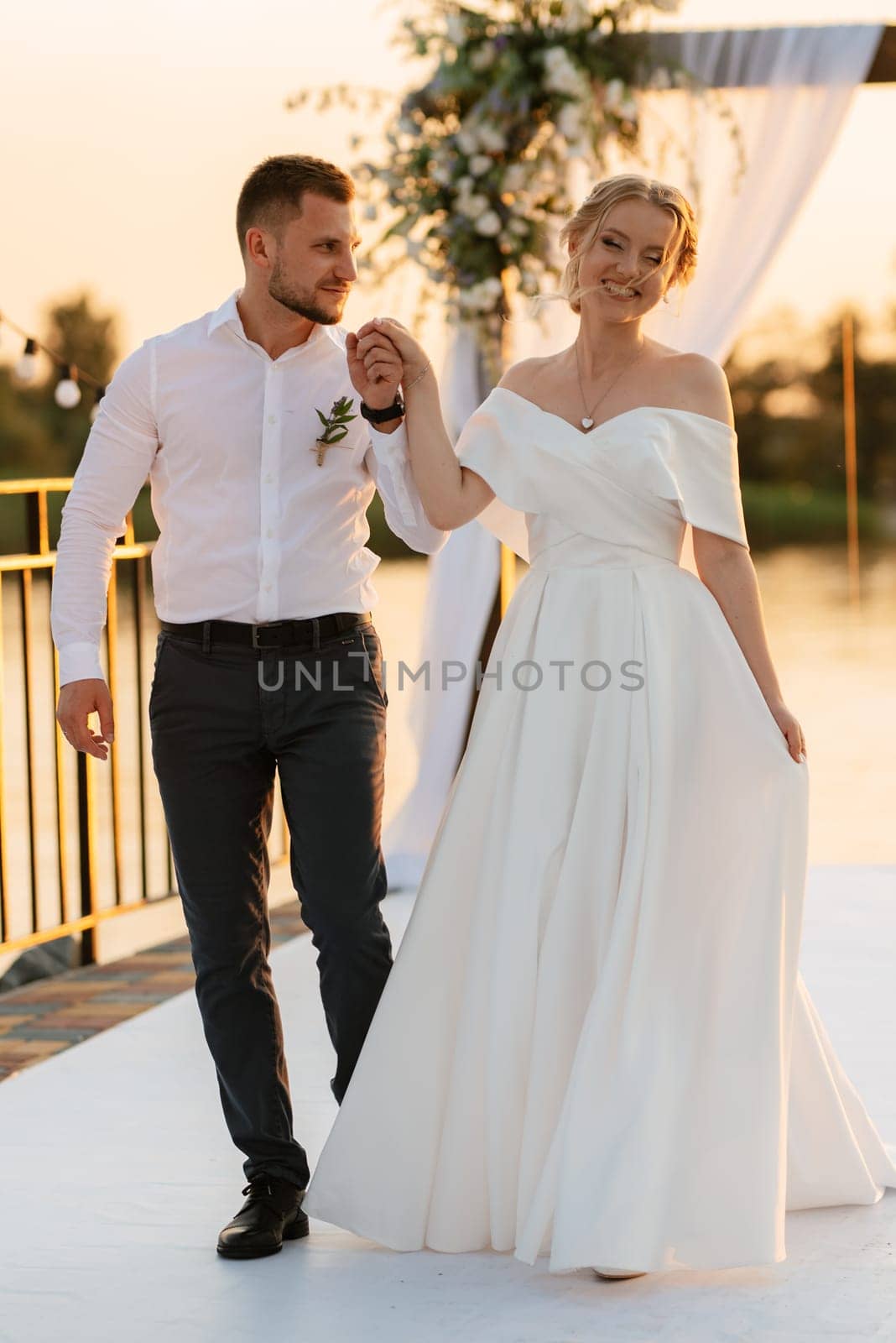 bride and groom against the backdrop of a yellow sunset on a pier near the river
