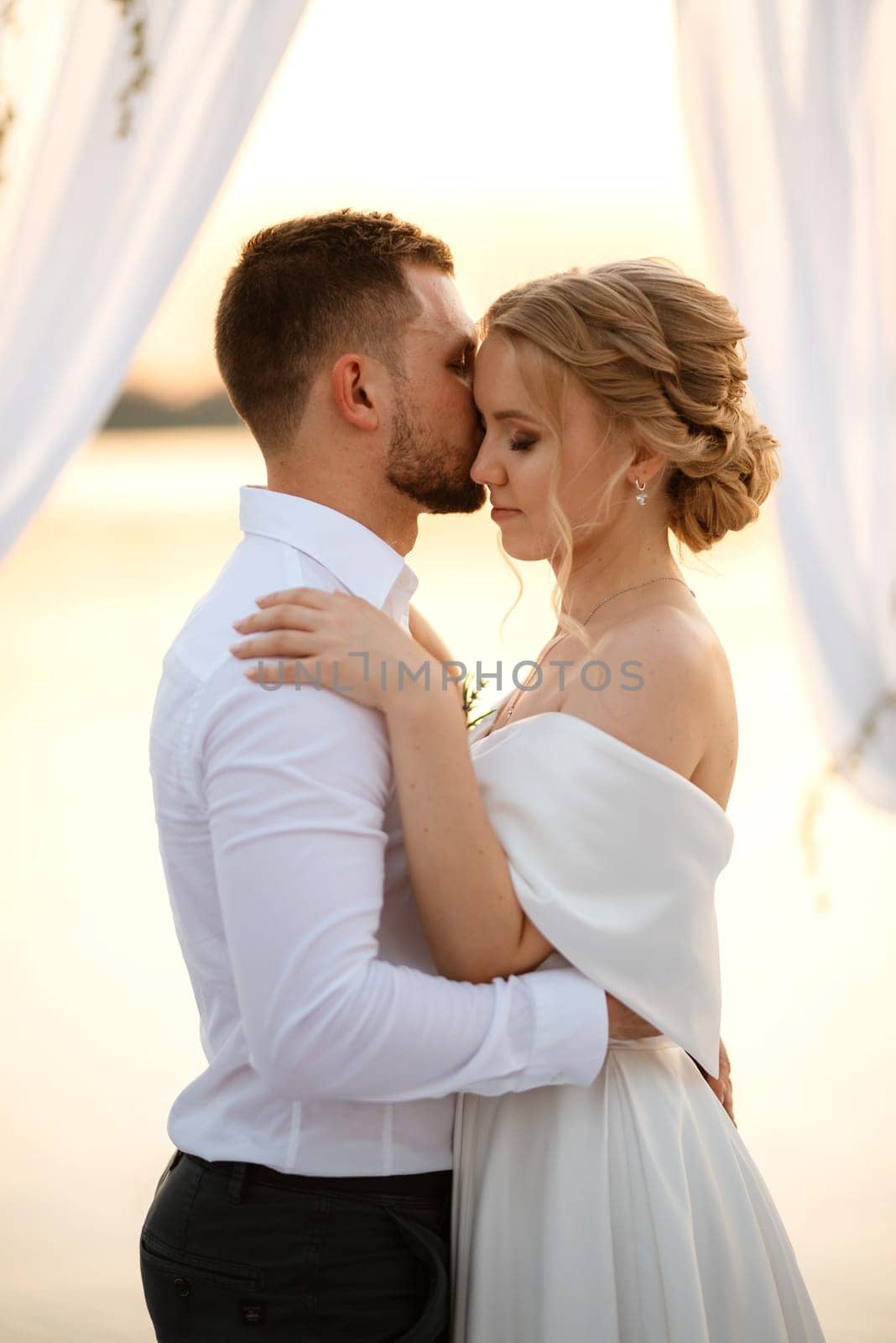 bride and groom against the backdrop of a yellow sunset on a pier near the river