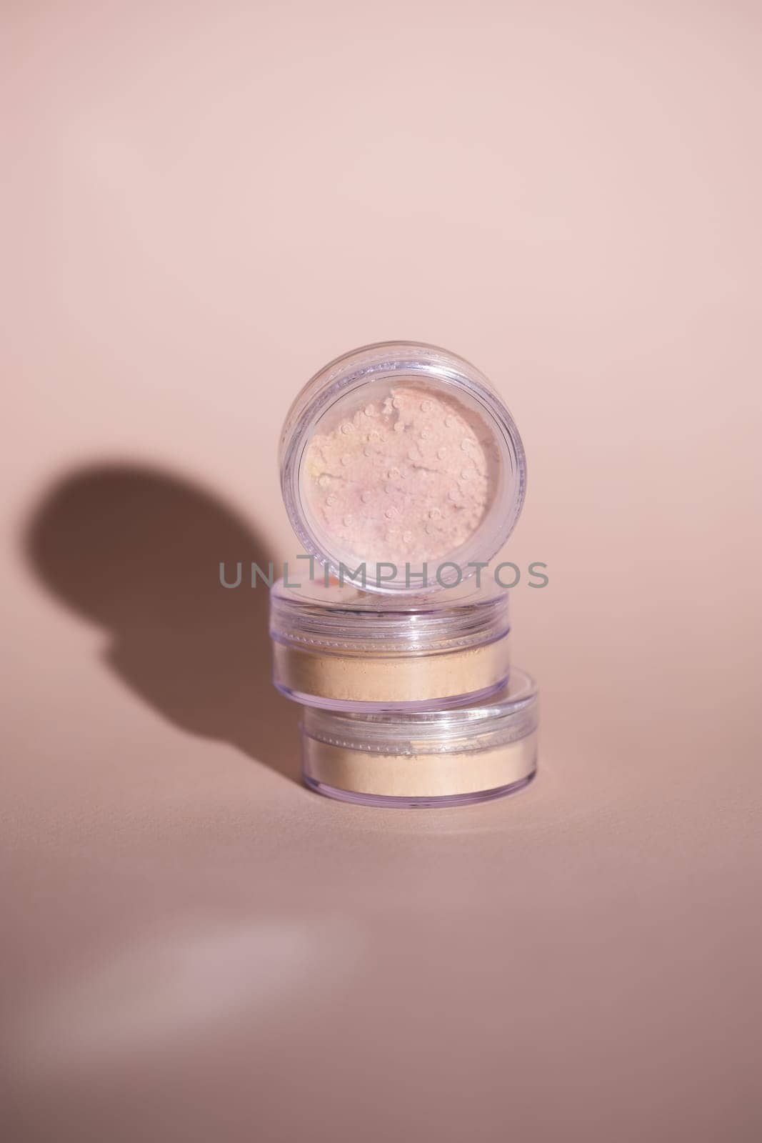 Mineral powder for skin tone color in small containers on pale rose colour background with shadows - beauty product and make up concept by Satura86