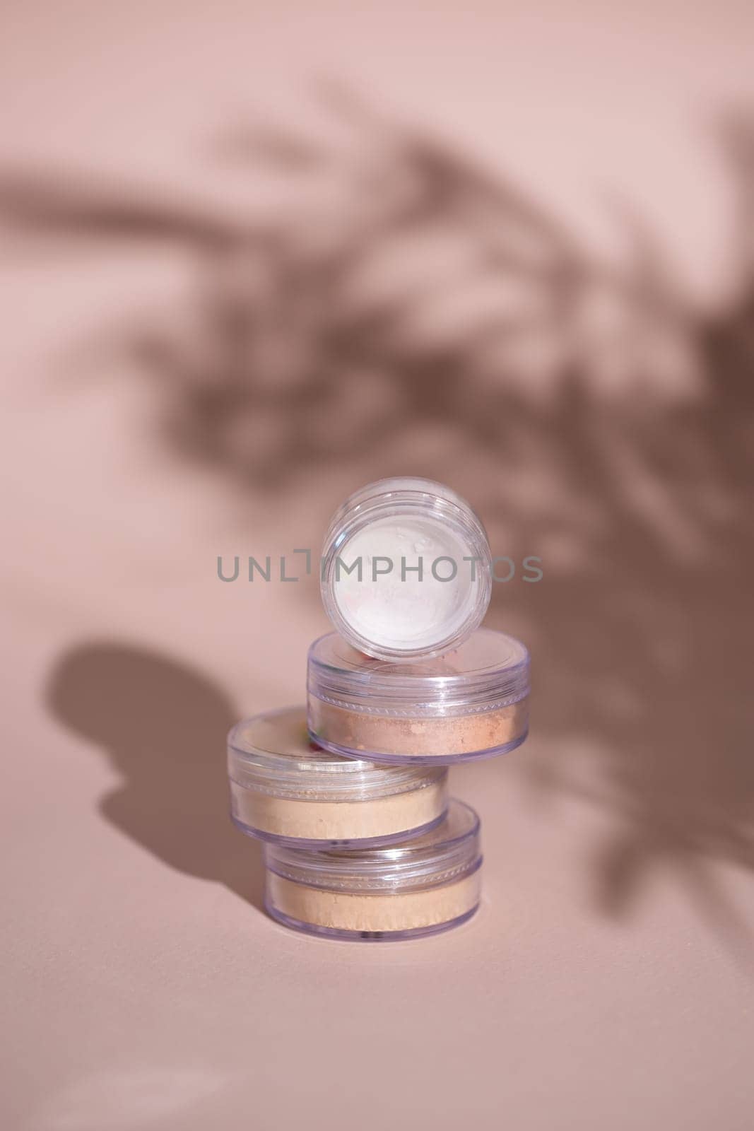 Mineral powder for skin tone color in small containers on pale rose colour background with shadows - beauty product and make up concept by Satura86