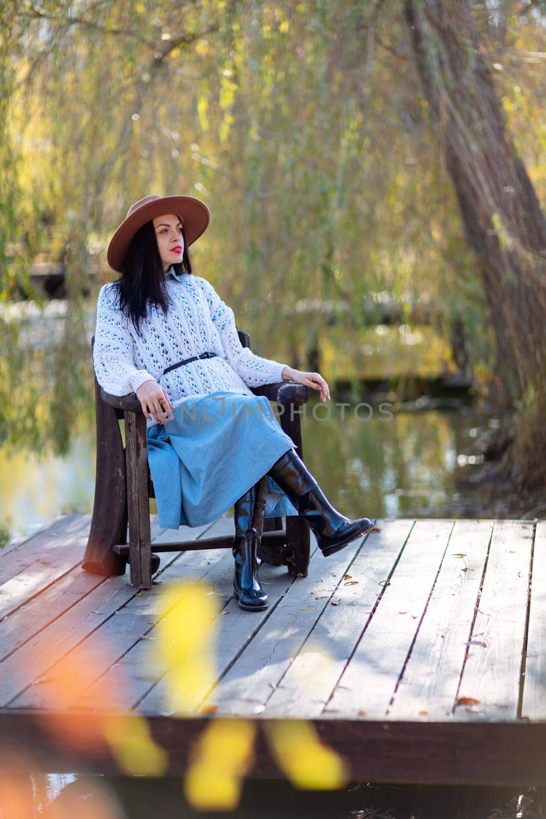 Autumn lake woman. She sits by a pond on a wooden pier in autumn and admires nature. The concept of tourism, weekends outside the city