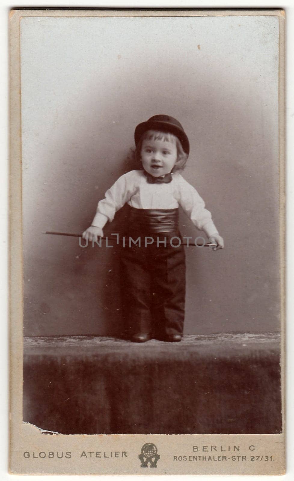 Vintage cabinet card shows cute small boy wears bowler hat, bow tie, cummerbund and holds walking stick. Antique black white photo. by roman_nerud
