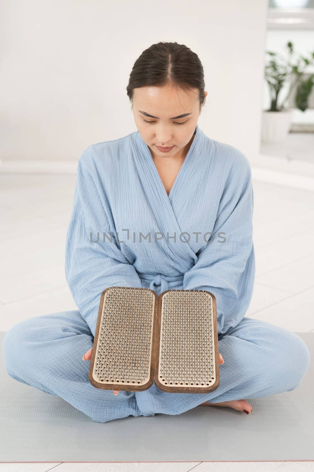 Asian woman sitting in lotus position on yoga mat and holding sadhu boards