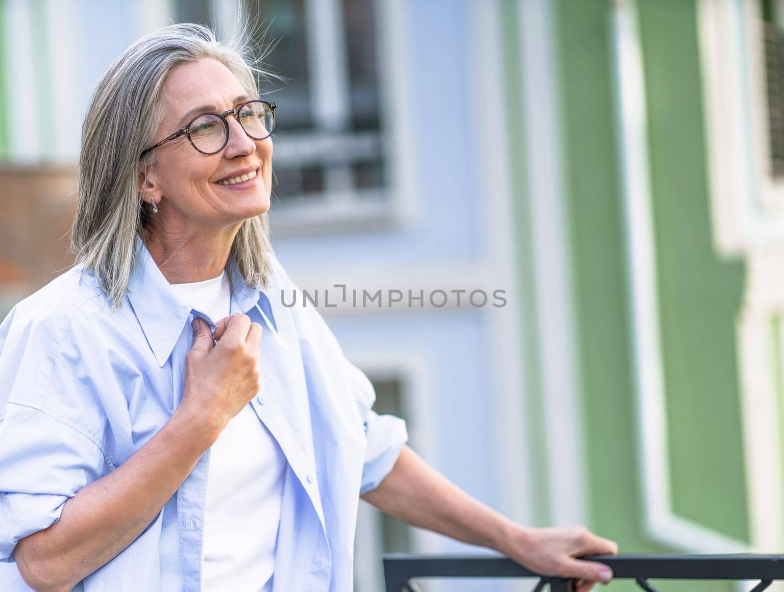 Concept of happiness with senior woman smiling with closed eyes in old city. Cheerful woman enjoying cityscape, outdoor, travel, tourism, vacation, leisure, relaxation, serenity, and calm atmosphere. High quality photo