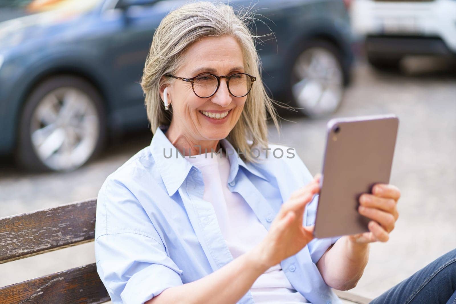 Happy and confident mature woman smiles while holding tablet PC and taking call in busy city. The urban scene and modern technology convey sense of connectivity and convenience, while the woman's positive energy and independent spirit inspire success and vibrancy. High quality photo