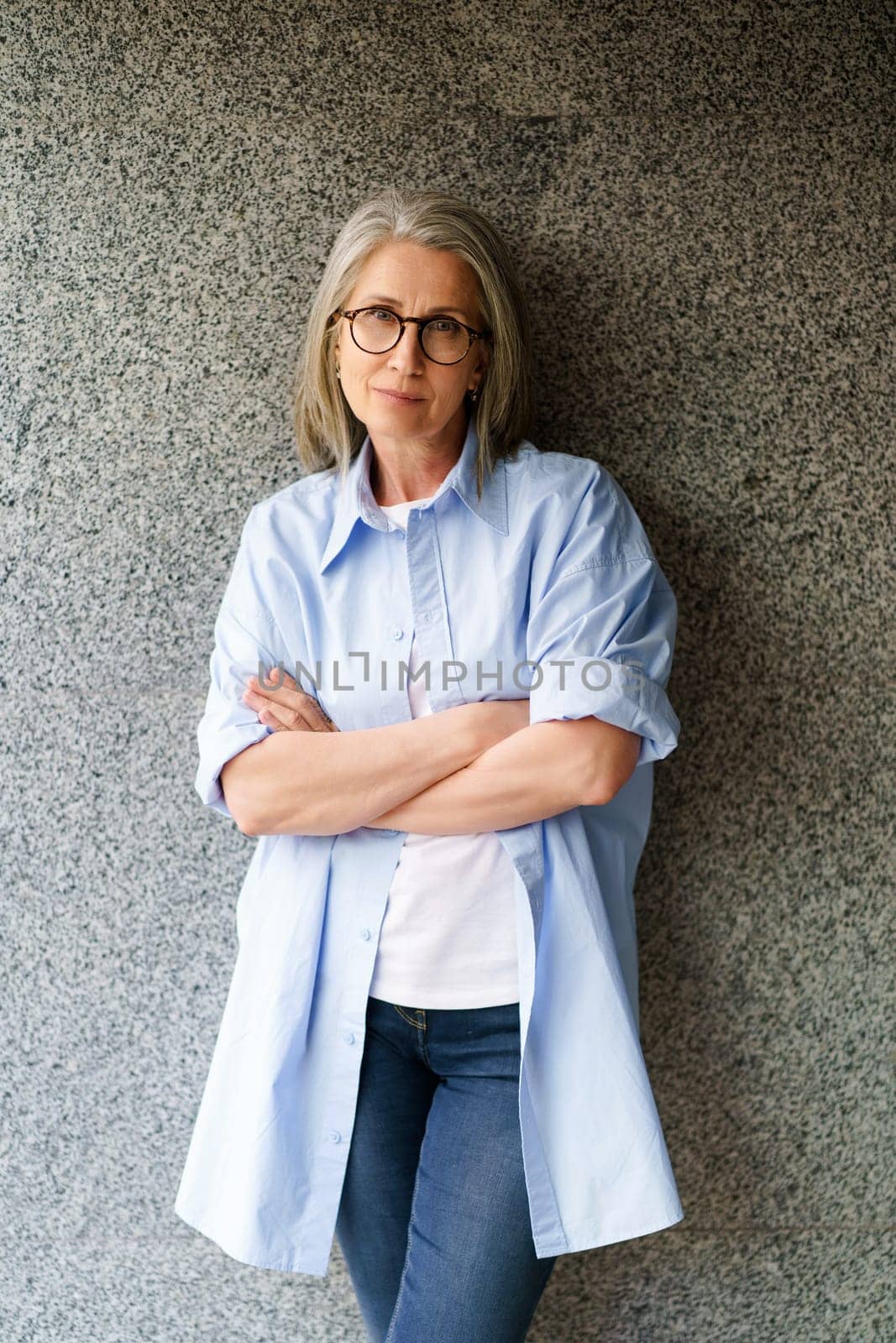 Confident and stylish senior woman with a seductive look standing near a wall in an urban environment, exuding independence and sophistication. High quality photo