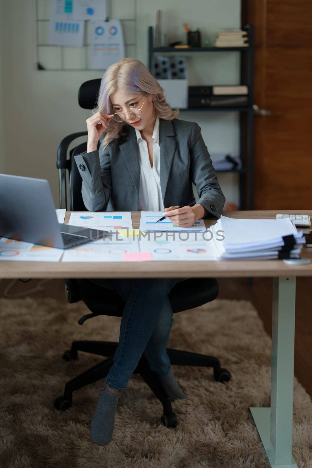 Portrait of a thoughtful Asian businesswoman looking at financial statements and making marketing plans using a computer on her desk.