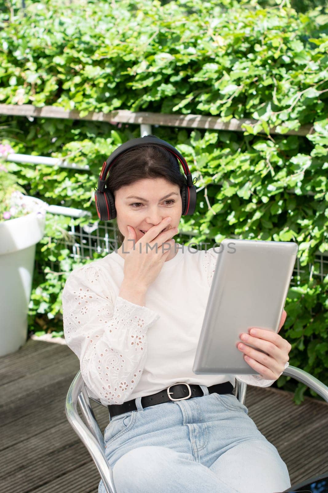candid portrait a young woman chatting through a tablet with headphones outdoor by KaterinaDalemans