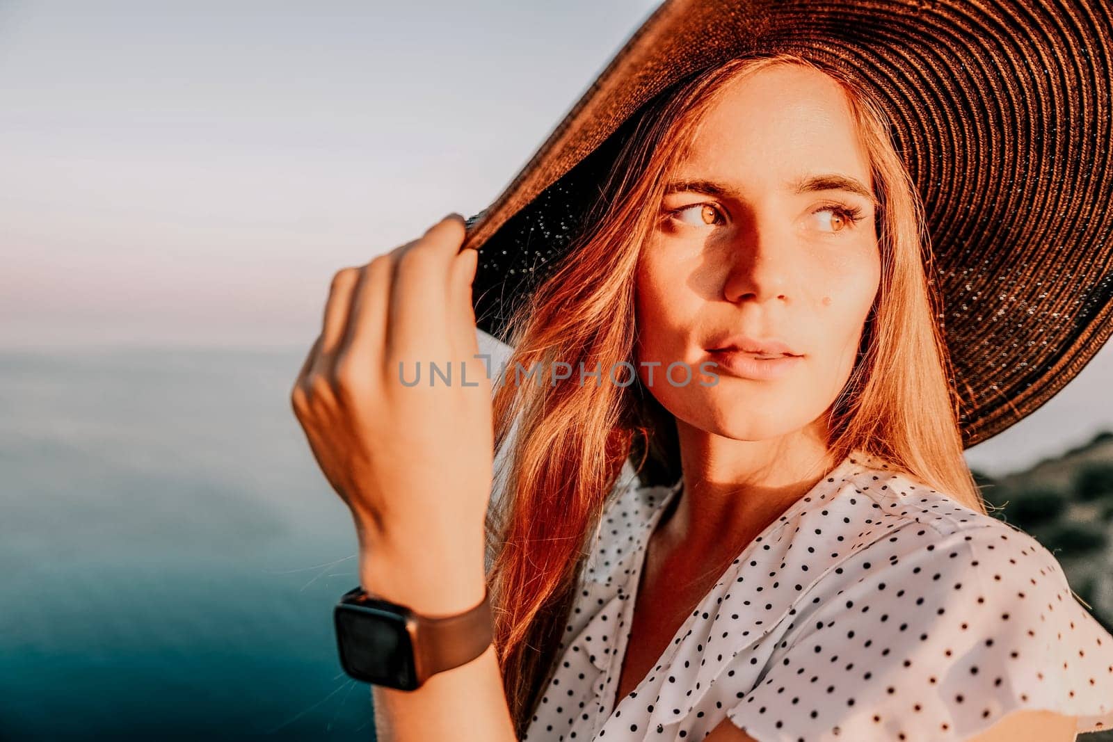 Portrait of happy young woman wearing summer black hat with large brim at beach on sunset. Closeup face of attractive girl with black straw hat. Happy young woman smiling and looking at camera at sea