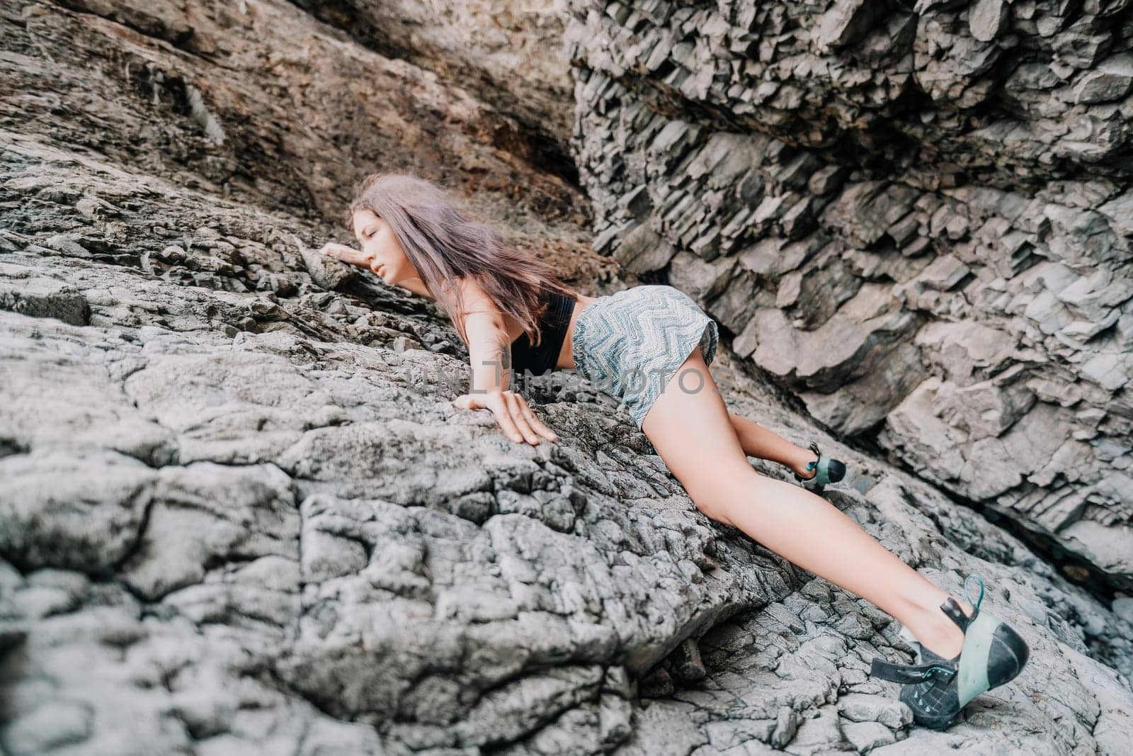 A girl climbs a rock. The athlete trains in nature. Woman overcomes difficult climbing route. Extreme hobby. Tourist woman rock climber hiking on mountains rocks over beautiful sea coast