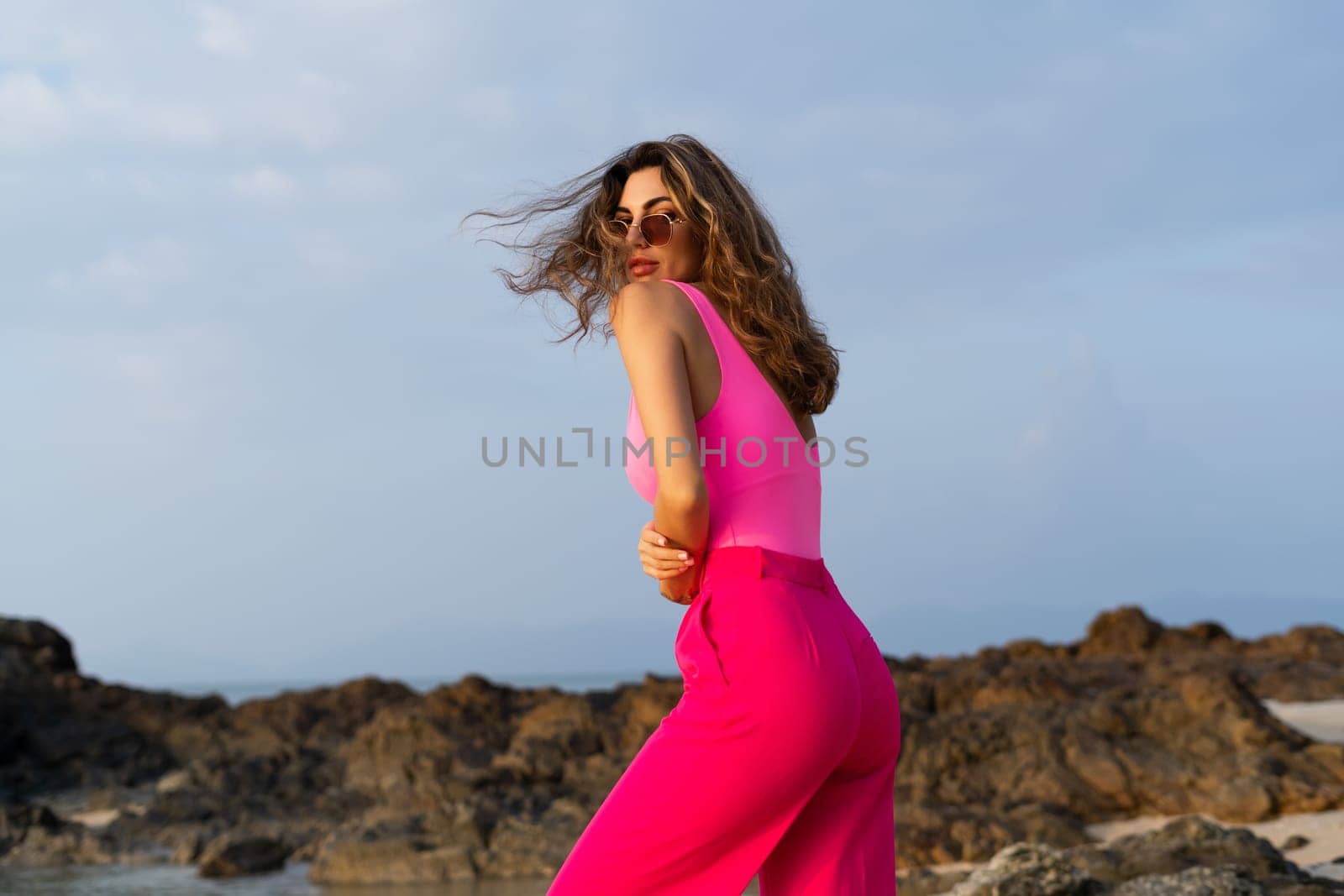 Fashion stylish beautiful sensual young woman, slim, in trendy bright pink pants and bodysuit on a tropical beach at sunset posing in sunglasses by kroshka_nastya