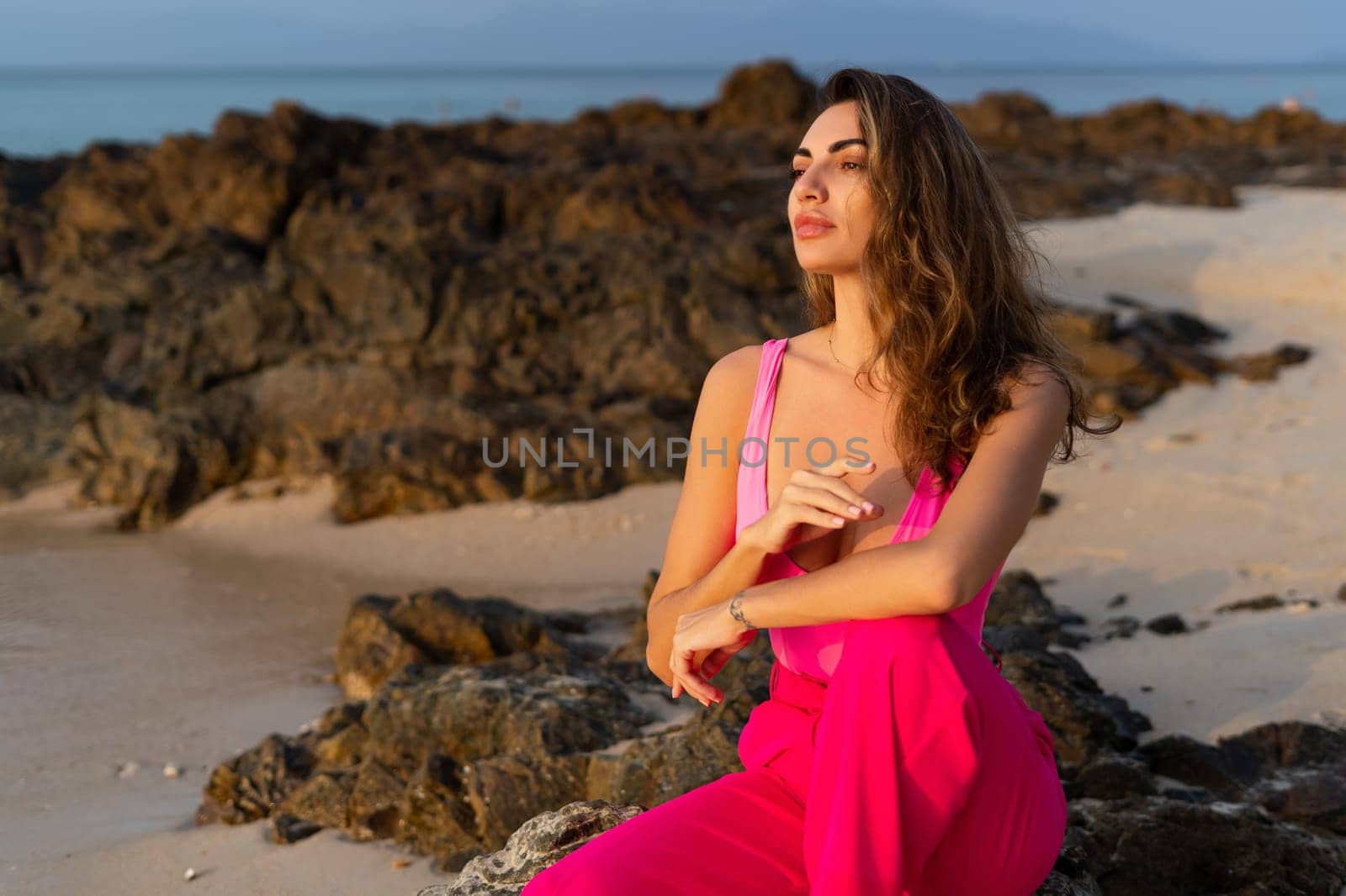 Fashion stylish beautiful sensual young woman, slim, in fashionable bright pink pants and bodysuit on a tropical beach at sunset posing