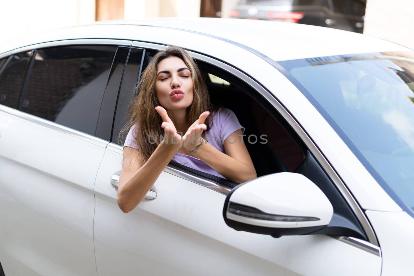 Beautiful young happy smiling woman driving her car, sitting behind the wheel, looking out the window, blow a kiss by kroshka_nastya