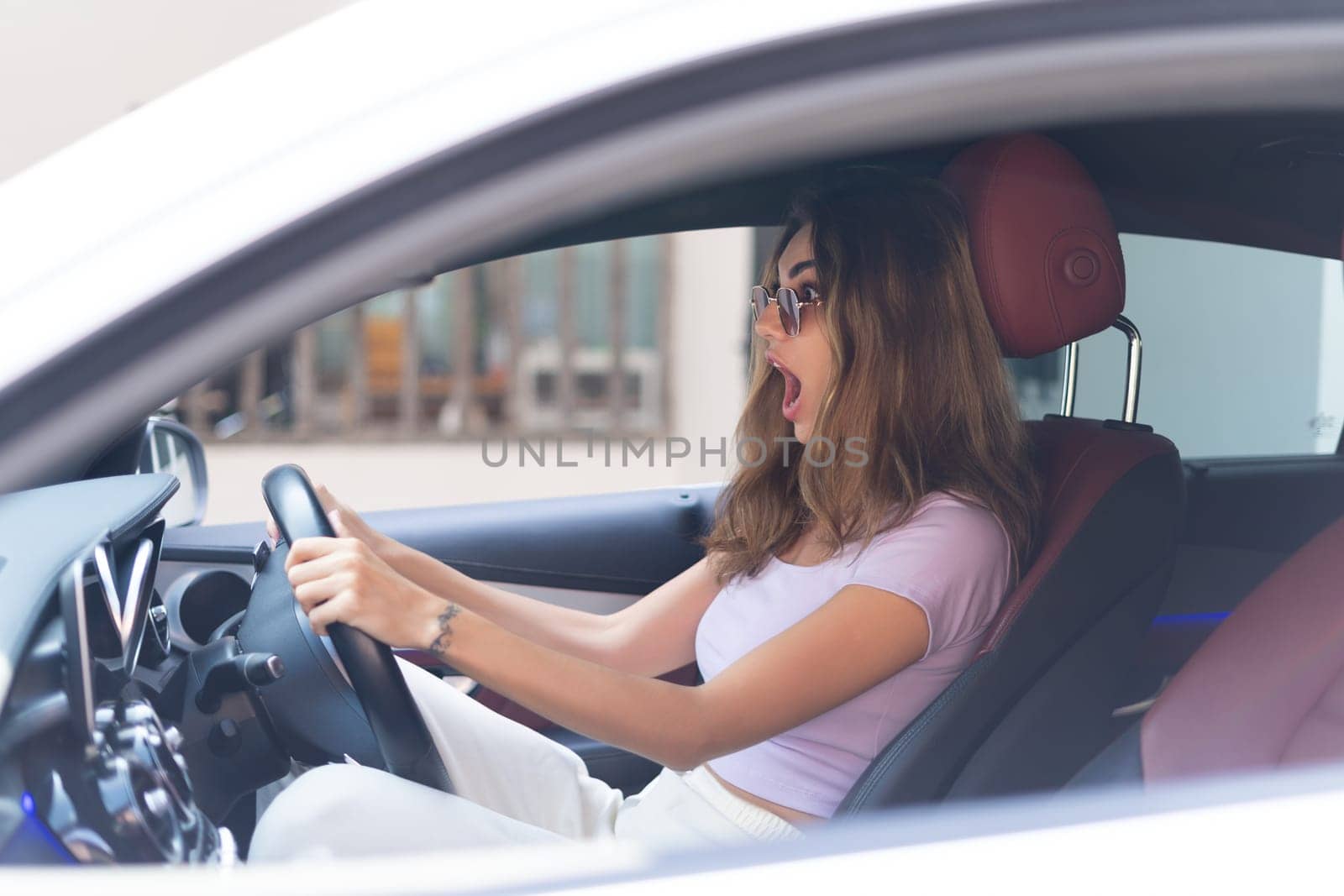 Beautiful young happy smiling woman driving her expensive luxury car, scared shocked with open mouth