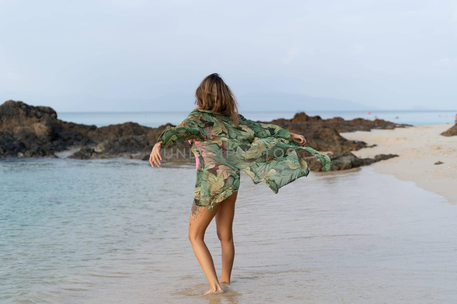 Stylish romantic tender athletic slim sensual woman in pink swimsuit, tropical kimono and sunglasses on the beach at sunset