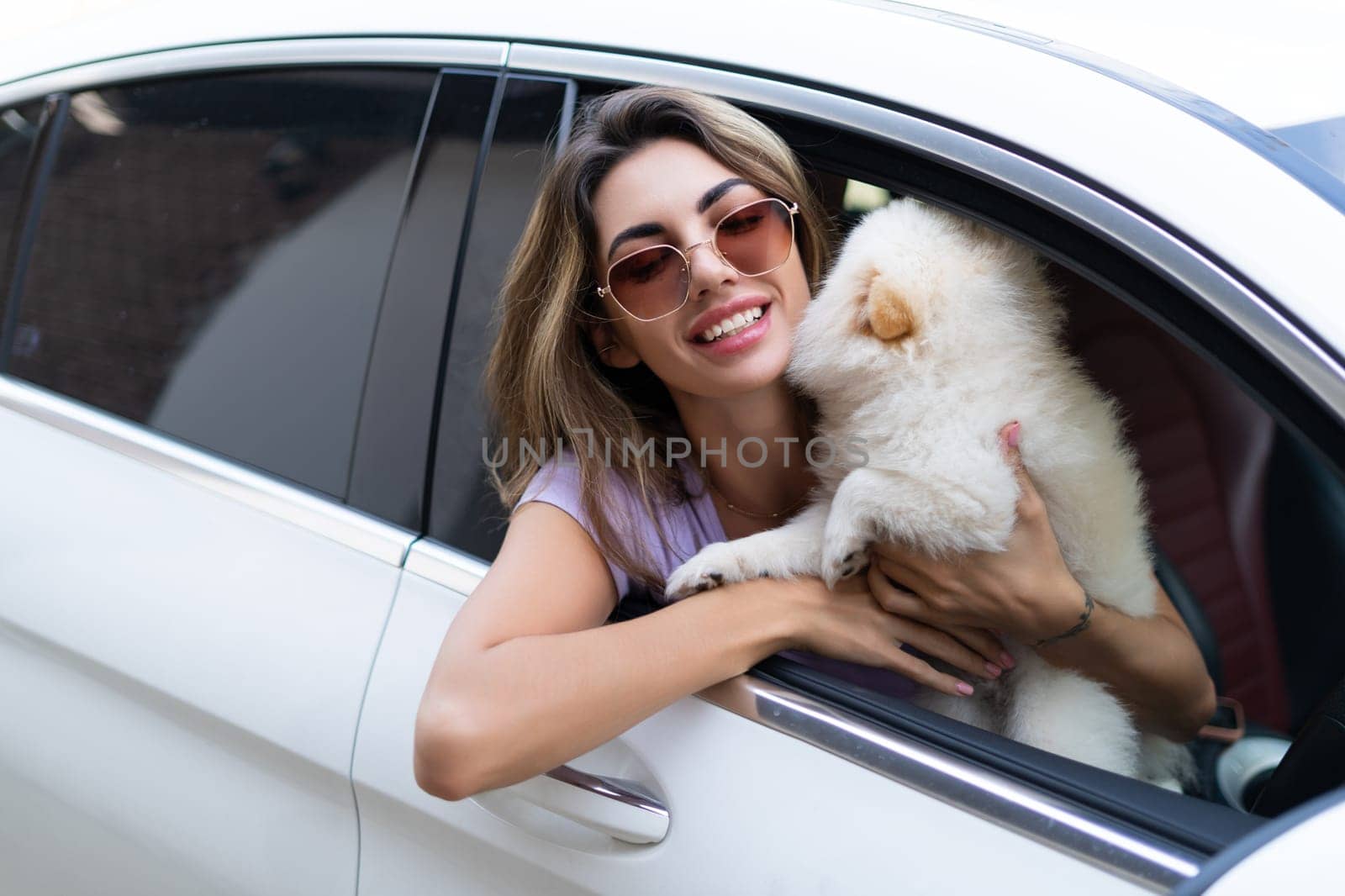 A happy woman and a dog in a car on a summer trip. Cute pomeranian spitz. Vacation with a pet. by kroshka_nastya