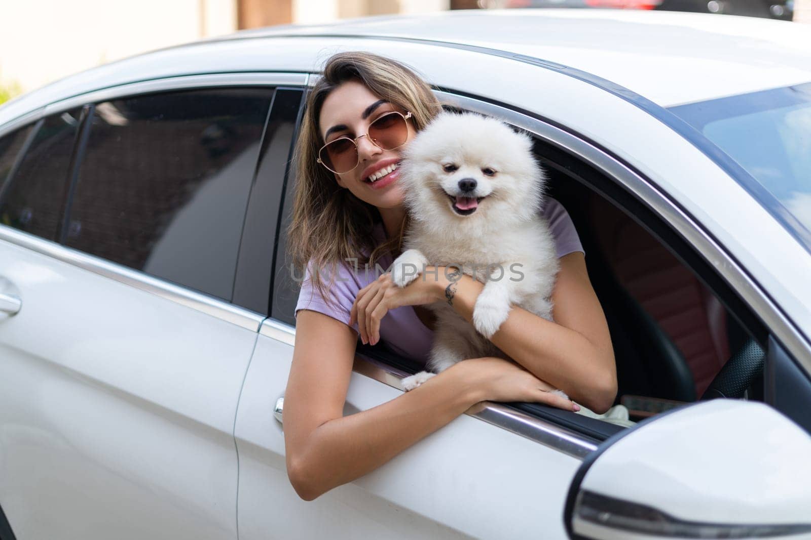 A happy woman and a dog in a car on a summer trip. Cute pomeranian spitz. Vacation with a pet.