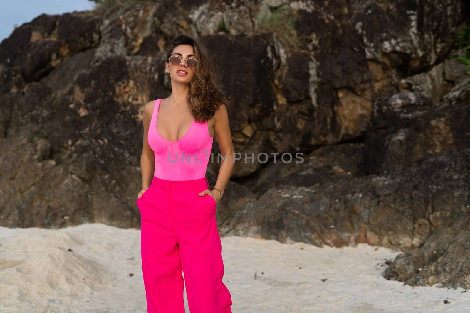 Fashion stylish beautiful sensual young woman, slim, in trendy bright pink pants and bodysuit on a tropical beach at sunset posing in sunglasses by kroshka_nastya