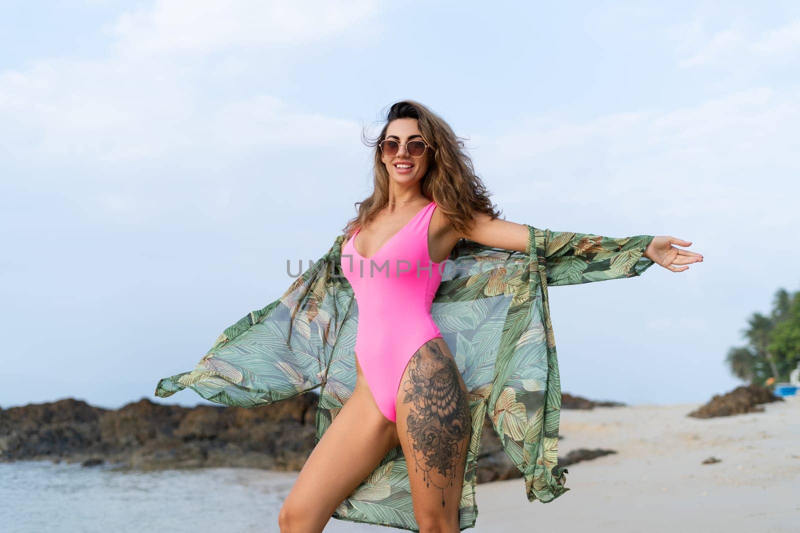 Stylish romantic tender athletic slim sensual woman in pink swimsuit, tropical kimono and sunglasses on the beach at sunset by kroshka_nastya