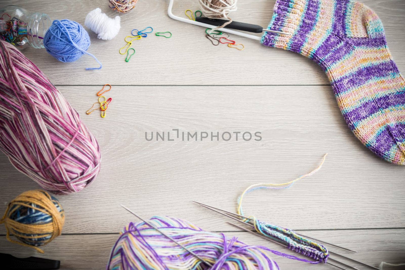 Colored threads, knitting needles and other items for hand knitting, on a light wooden table .