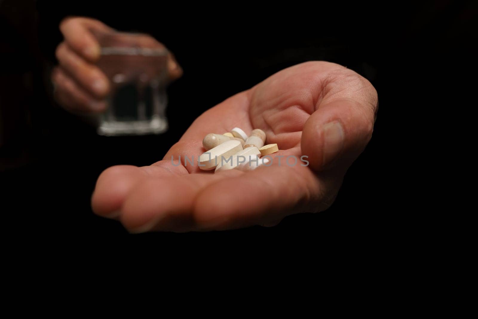 man with pills in one hand and a glass of water in the other black background by joseantona