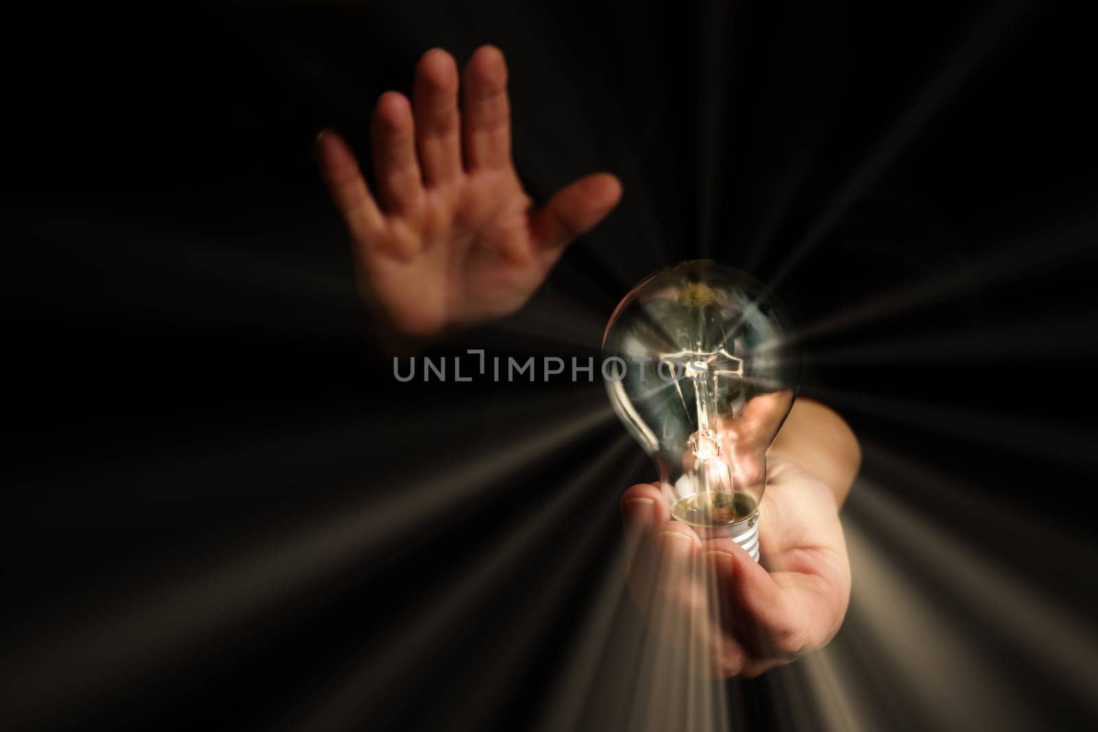 man holding in his hands a lighted light bulb with rays of light on a black background