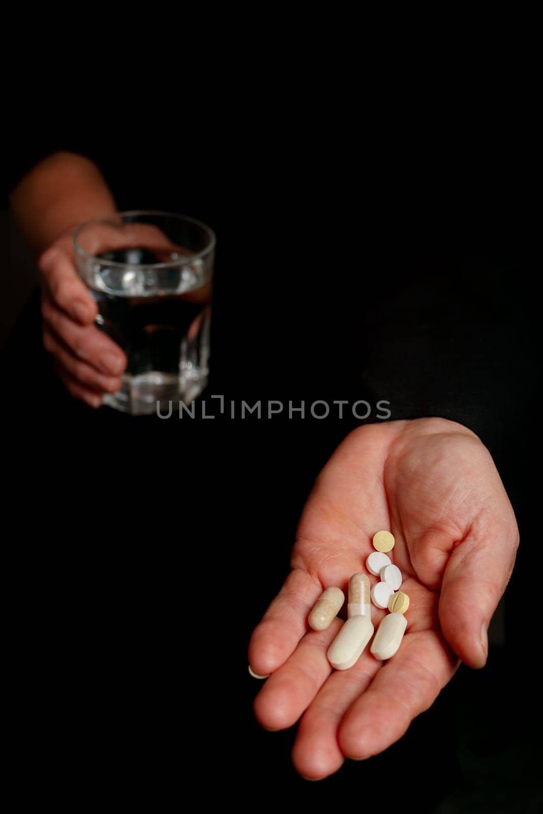 woman with pills in one hand and a glass of water in the other black background by joseantona