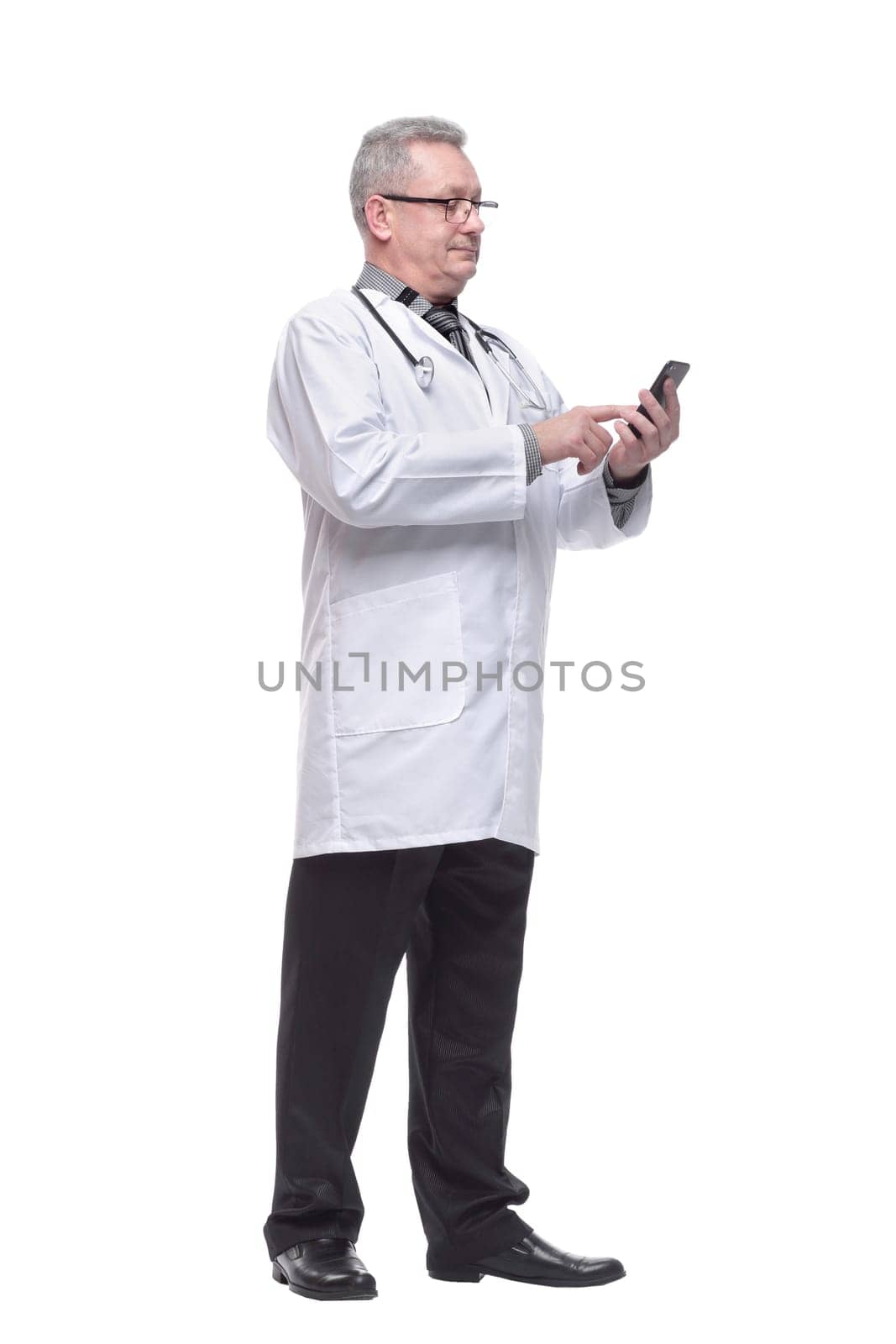 Closeup photo of man doctor standing isolated on white background looking attentively at screen of cellphone, smiling nicely