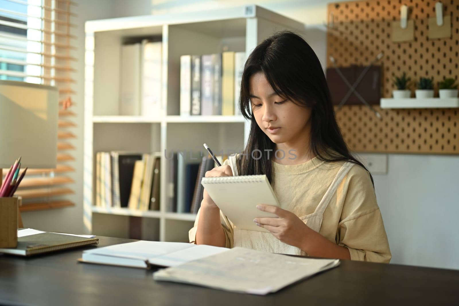 Concentred teenage asian woman doing homework, school project, preparing for exam at home.