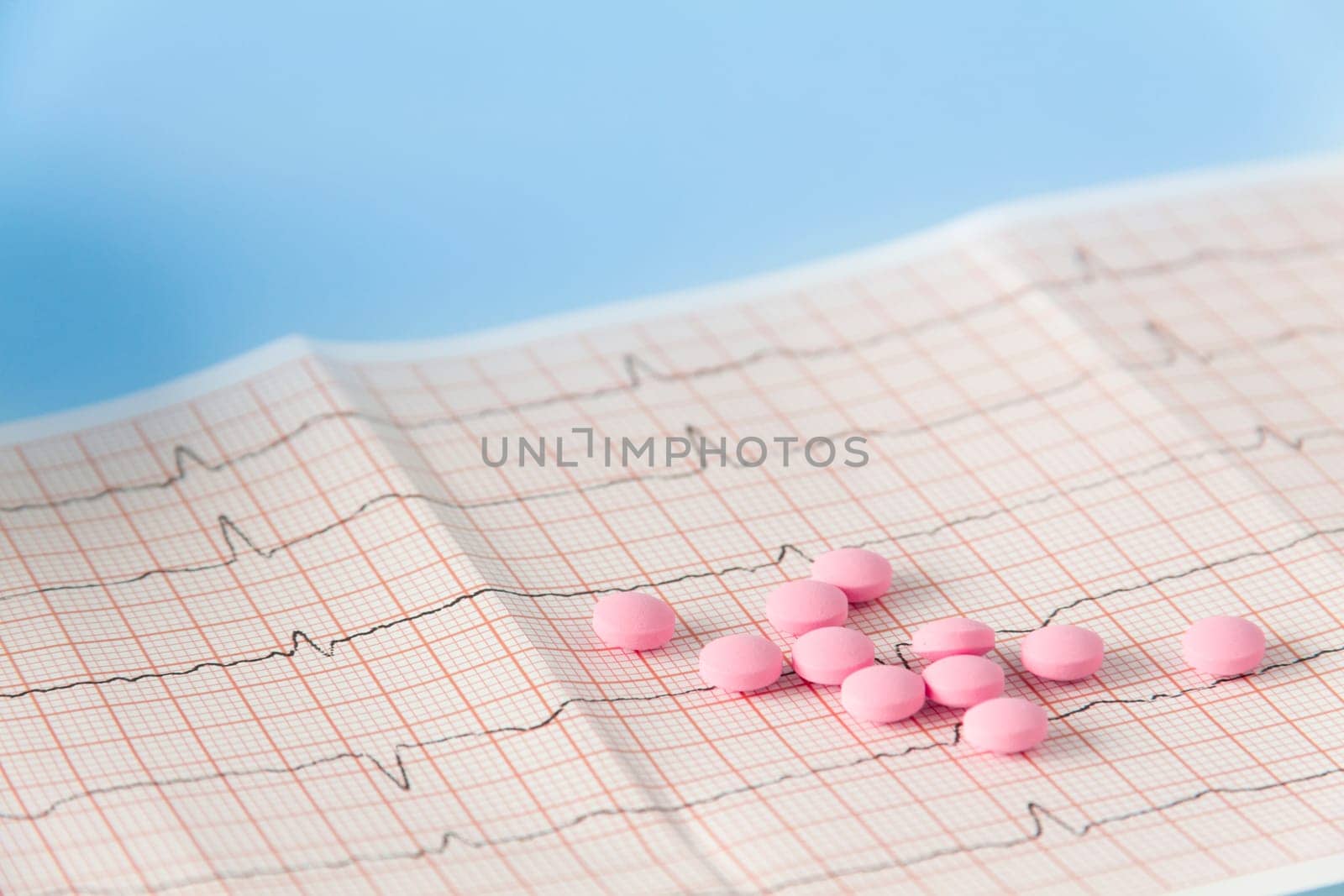 A large handful of pink pills lie on the electrocardiogram of the heart on a blue background. The concept of a healthy lifestyle and timely medical examination. by Alla_Yurtayeva