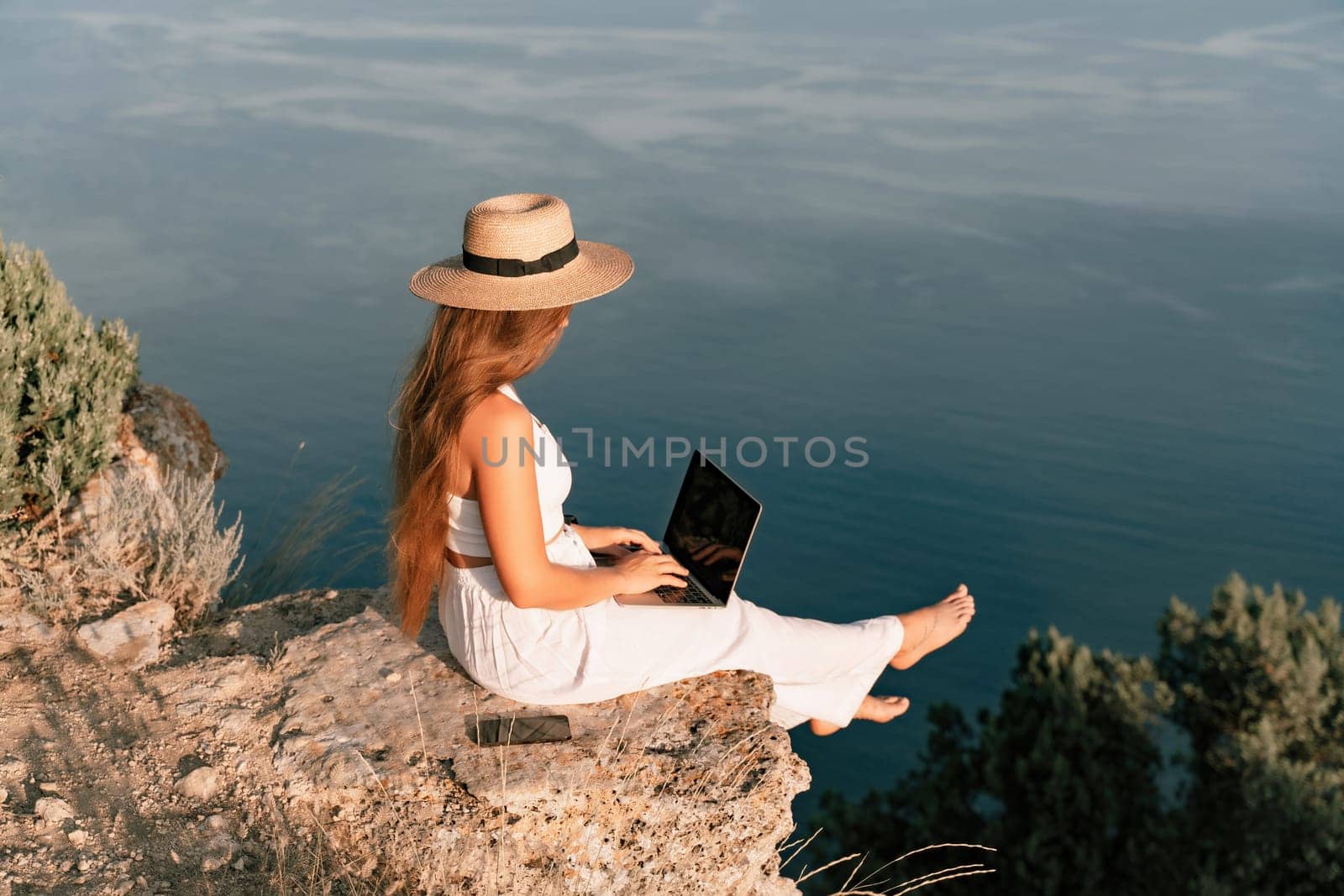 Freelance women sea working on the computer. Good looking middle aged woman typing on a laptop keyboard outdoors with a beautiful sea view. The concept of remote work