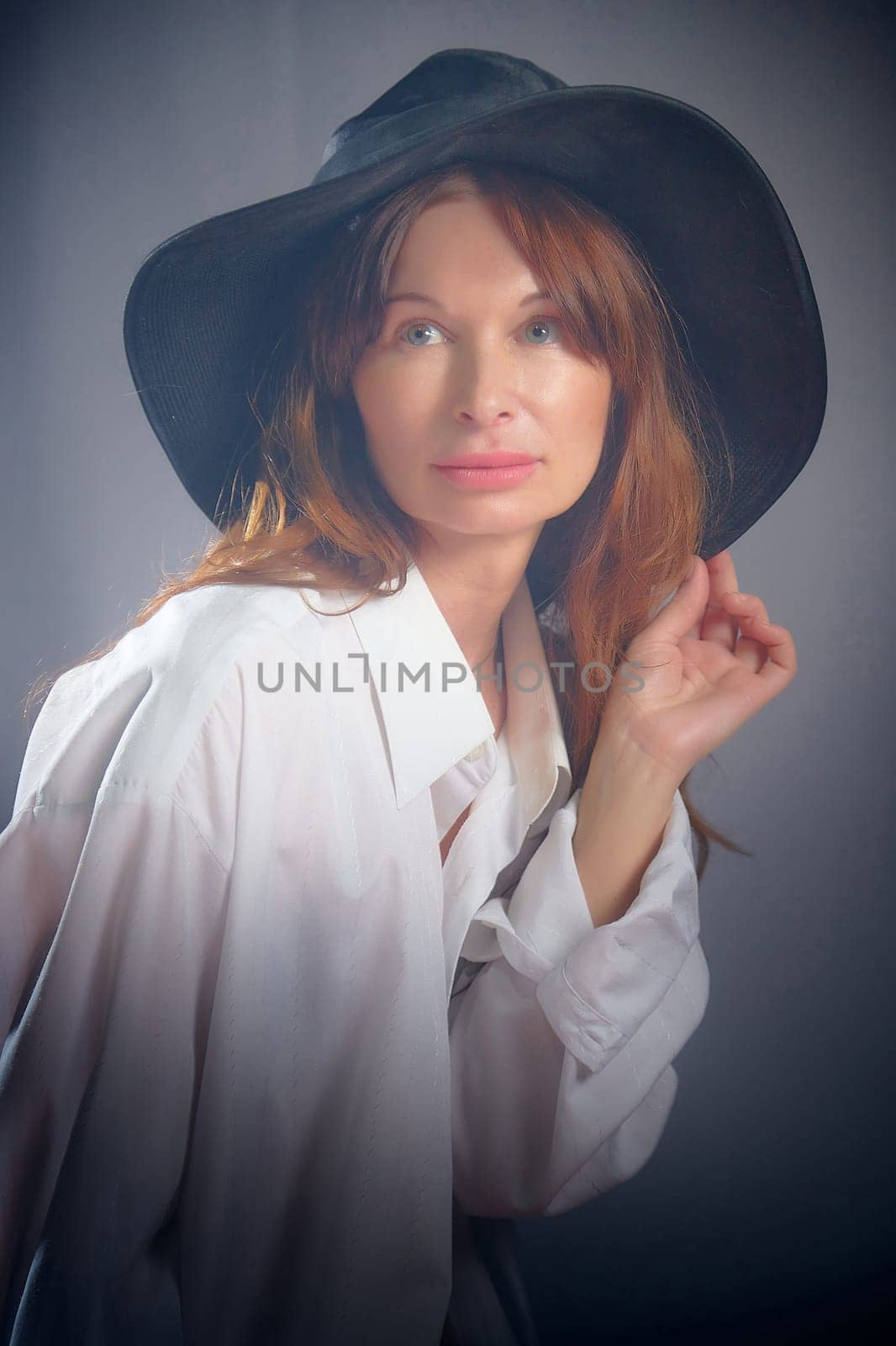 Portrait of a young sexy girl in white shirt and hat on a grey background. Classic style. dramatic portrait