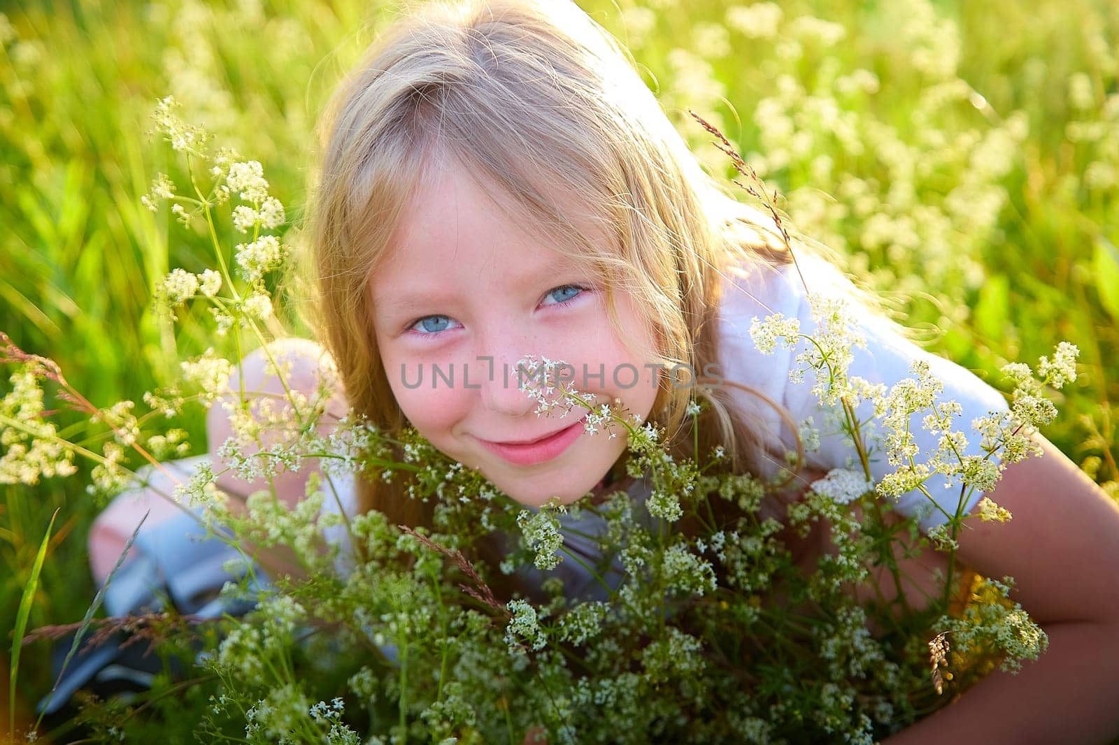 Portrait of pretty blonde girl having fun in a meadow on a natural landscape with grass and flowers on a sunny summer day. Portrait of a teenage child in summer or spring outdoors on field by keleny