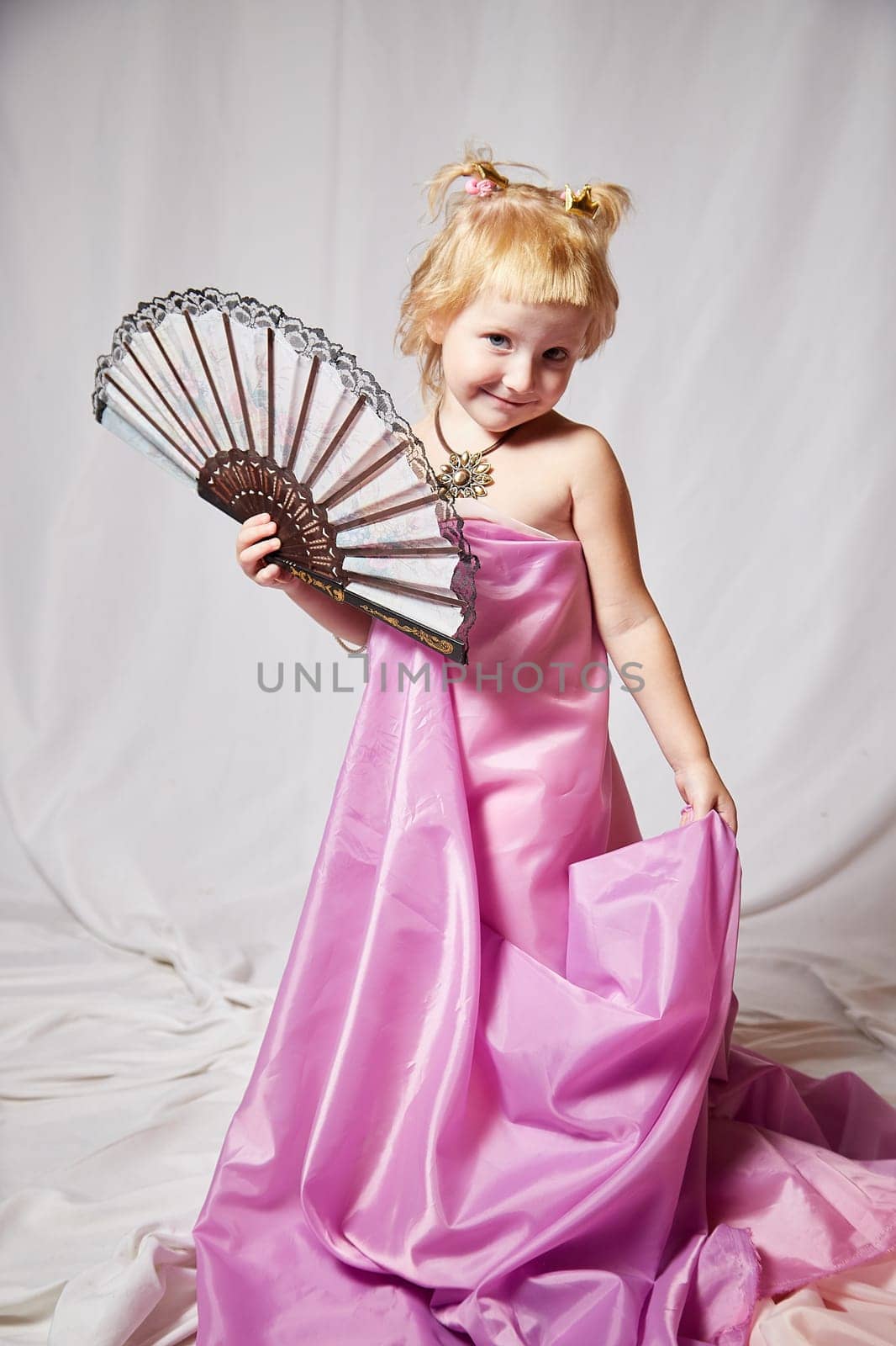 Portrait of cute kid girl posing in pink beautiful dress on a white background. Young female model looking as magic princess from fairy taly by keleny