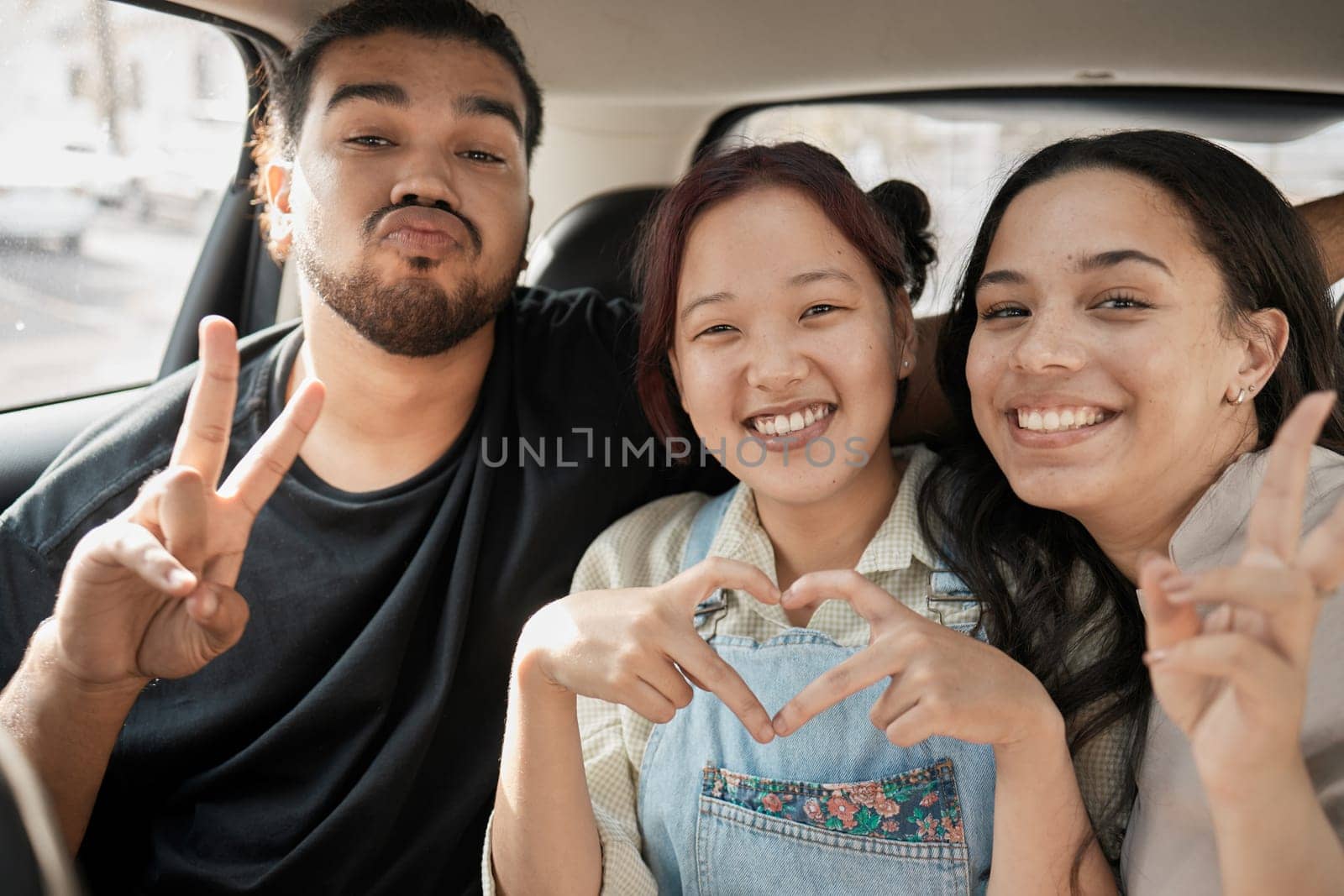Friends, road trip and hand gesture with a man and woman group making peace and heart shape sign in a car. Diversity, travel and transportation with a male and female friend bonding in a vehicle.