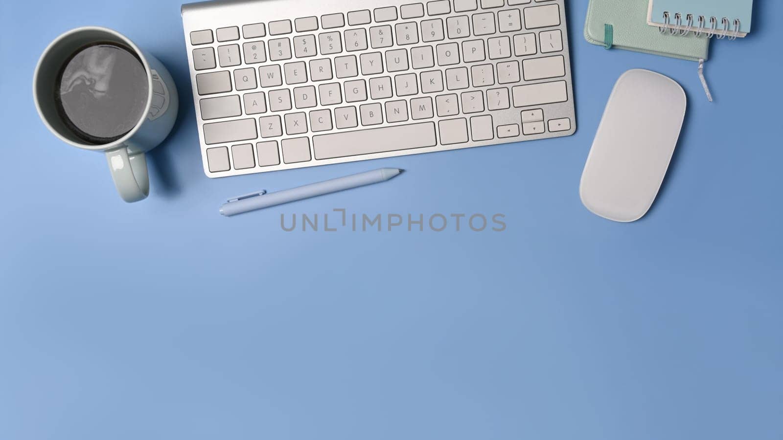 Top view wireless keyboard, coffee cup and notebook on blue background.