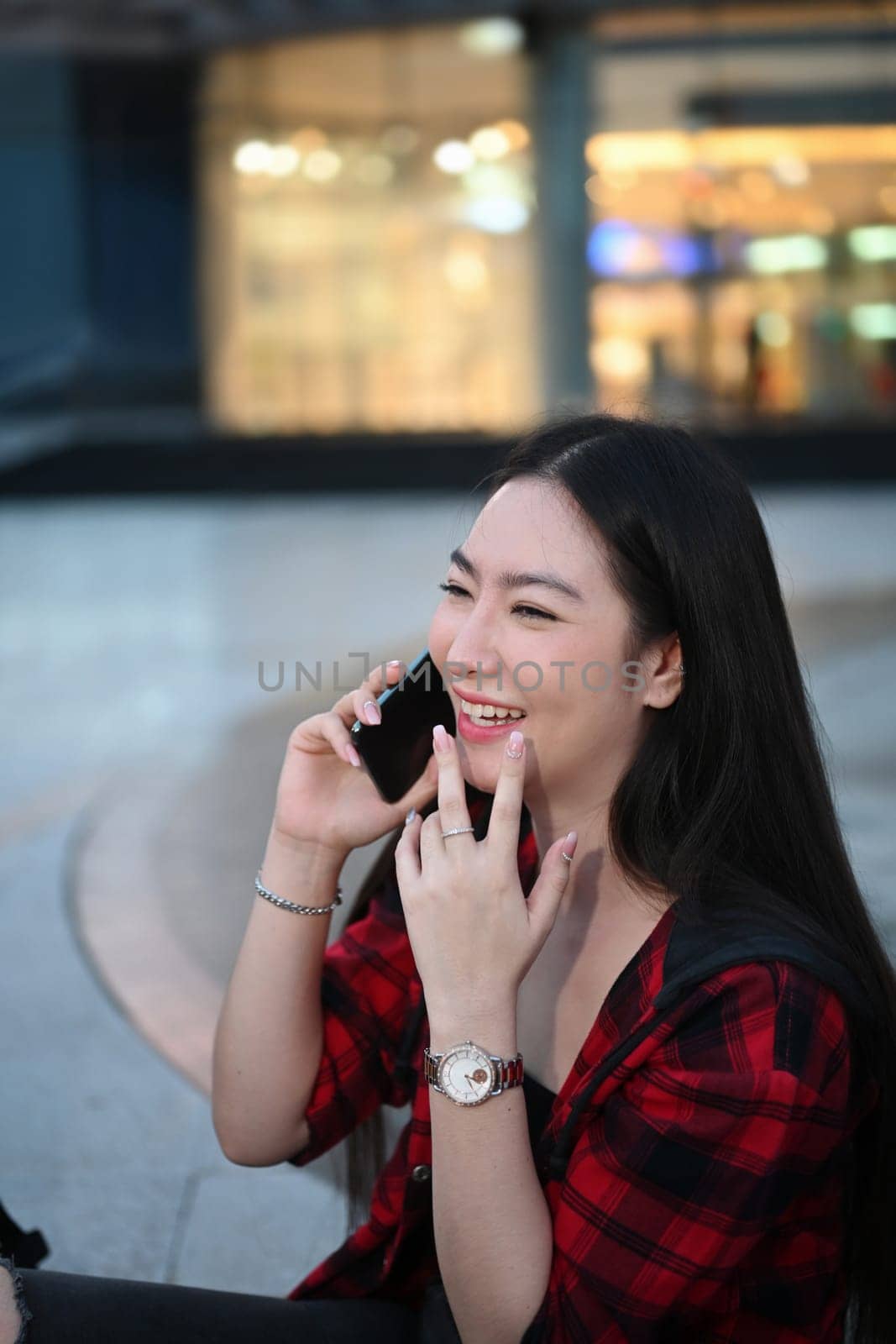 Happy Asian woman sitting in the city street at night and talking on mobile phone. by prathanchorruangsak