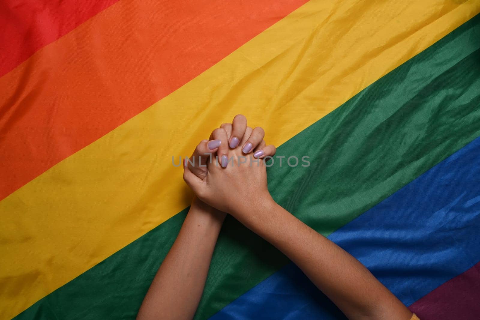 Two women lesbian couple holding hands over LGBT pride flag. LGBT concept. by prathanchorruangsak