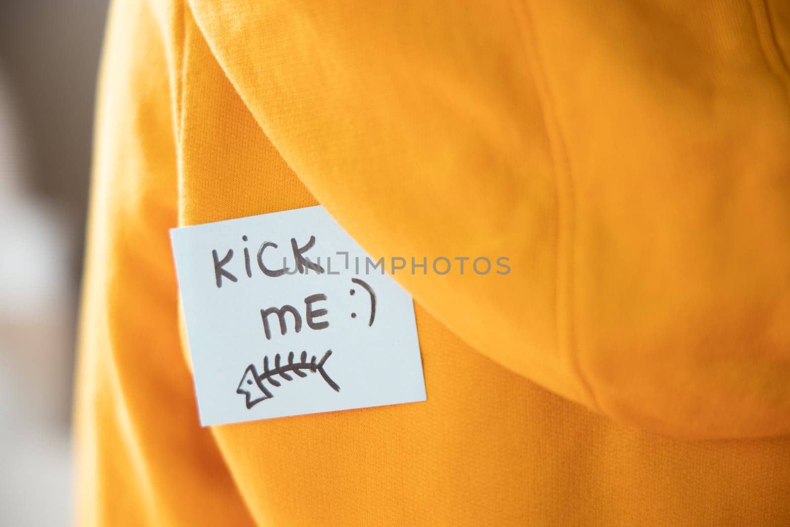 Sticky paper on yellow with text KICK ME and fish on back, closeup. April fools day concept. by Ri6ka