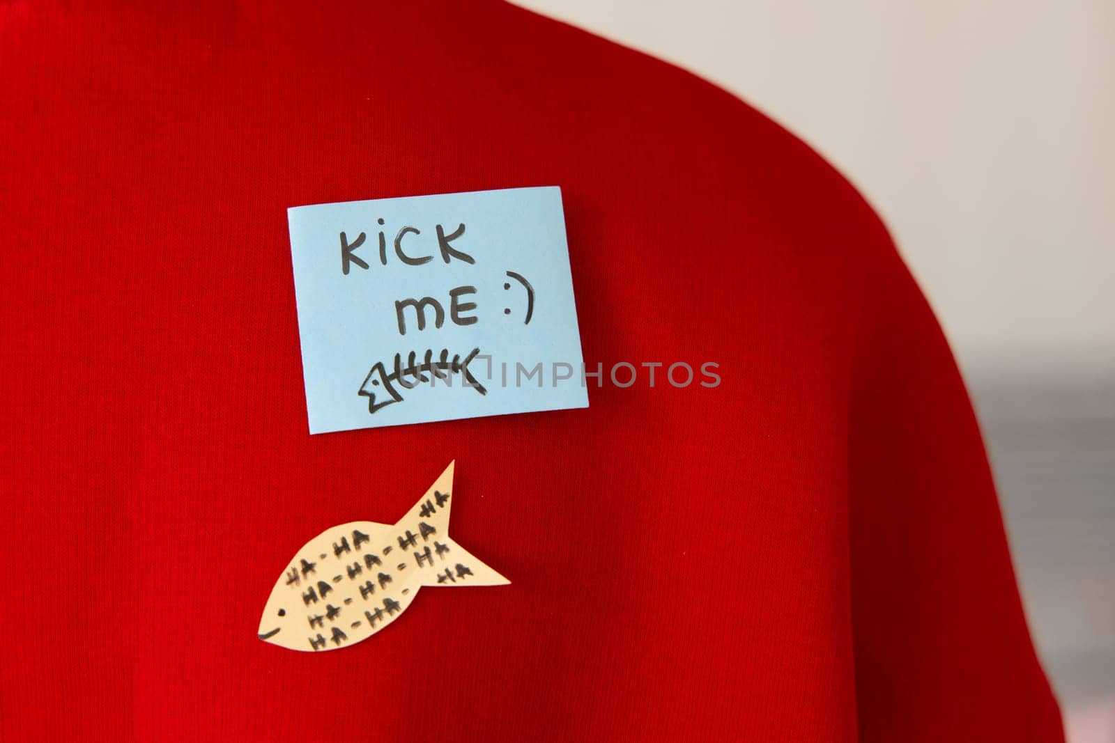 Boy in red hoodie with a sticky note on his back, saying kick me. Fools day concept.