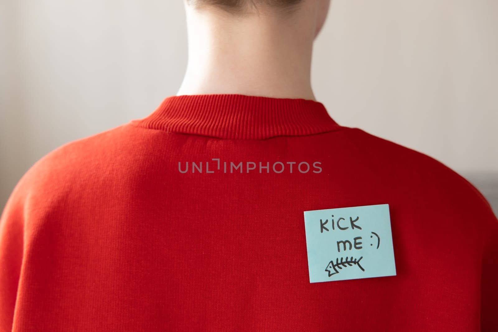 Boy in red hoodie with a sticky note on his back, saying kick me.