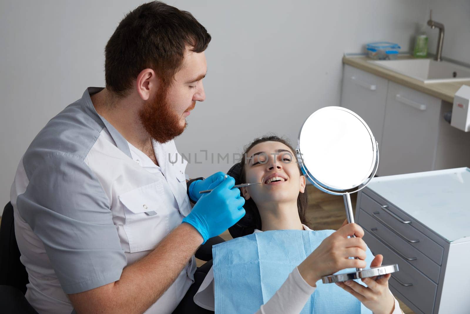 Young Woman checking her beautiful smile in mirror after stomatological treatment by Mariakray