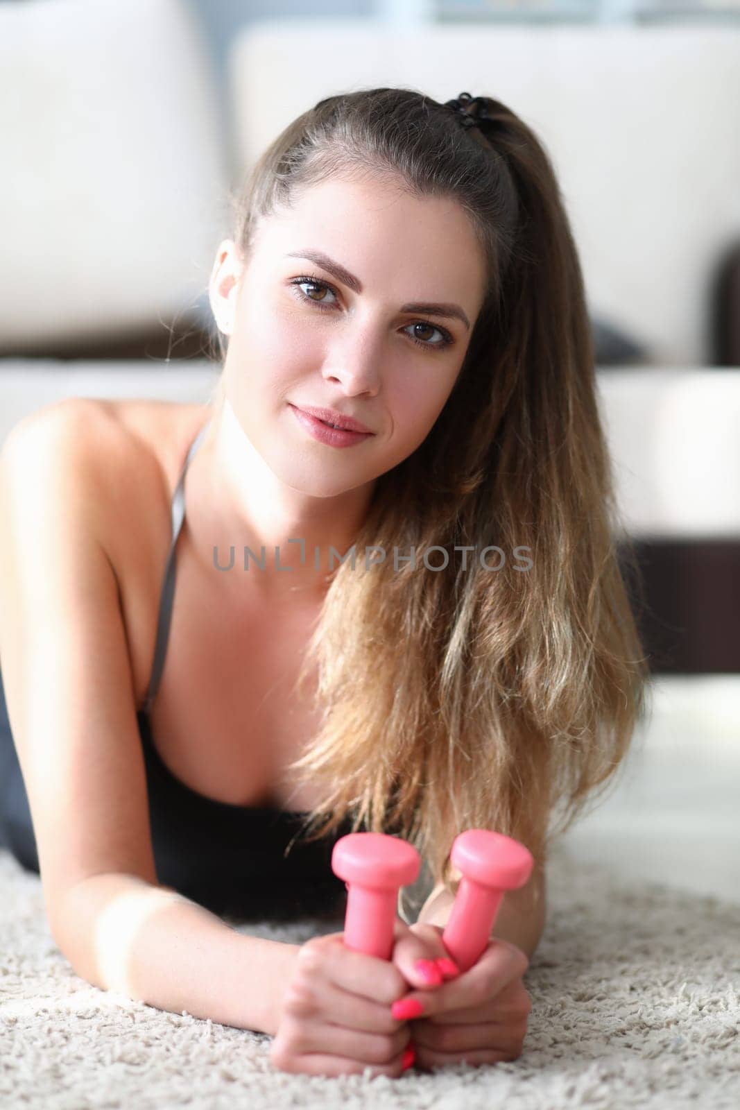 Portrait of beautiful young woman lies on floor with dumbbells. Home fitness and health concept