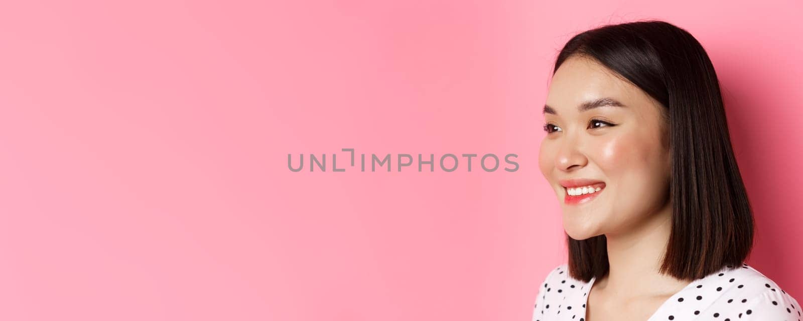 Beauty and skin care concept. Profile of beautiful asian girl smiling and looking happy left, standing against pink background by Benzoix