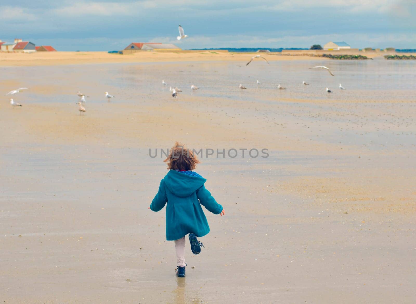 Girl in a green coat run away. Seagulls flying around at a Atlantic ocean