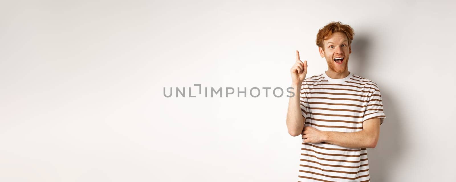 Young man with red hair having an idea, raising finger to say suggestion, standing happy over white background by Benzoix