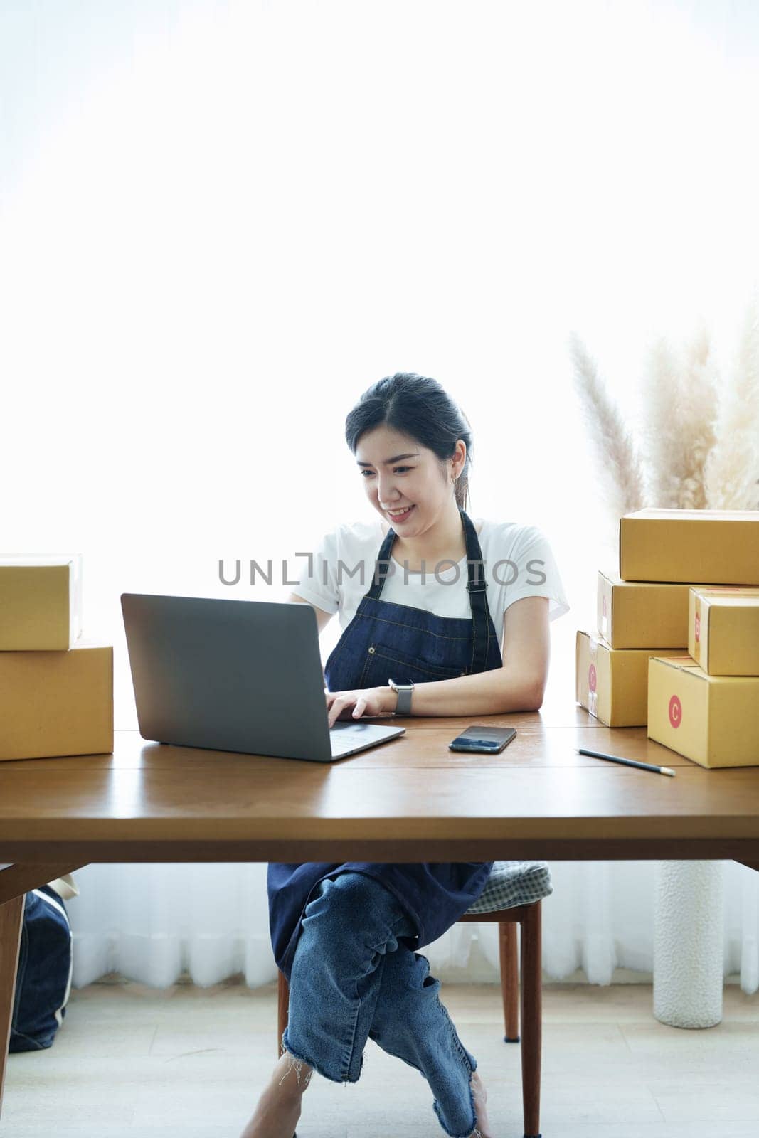 Starting small business entrepreneur of independent Asian woman smiling using laptop computer with cheerful success of online marketing package box items and SME delivery concept.