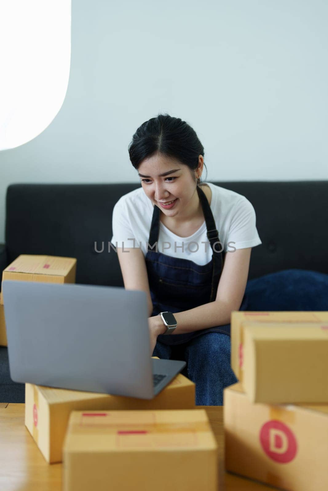 Starting small business entrepreneur of independent Asian woman smiling using laptop computer with cheerful success of online marketing package box items and SME delivery concept.