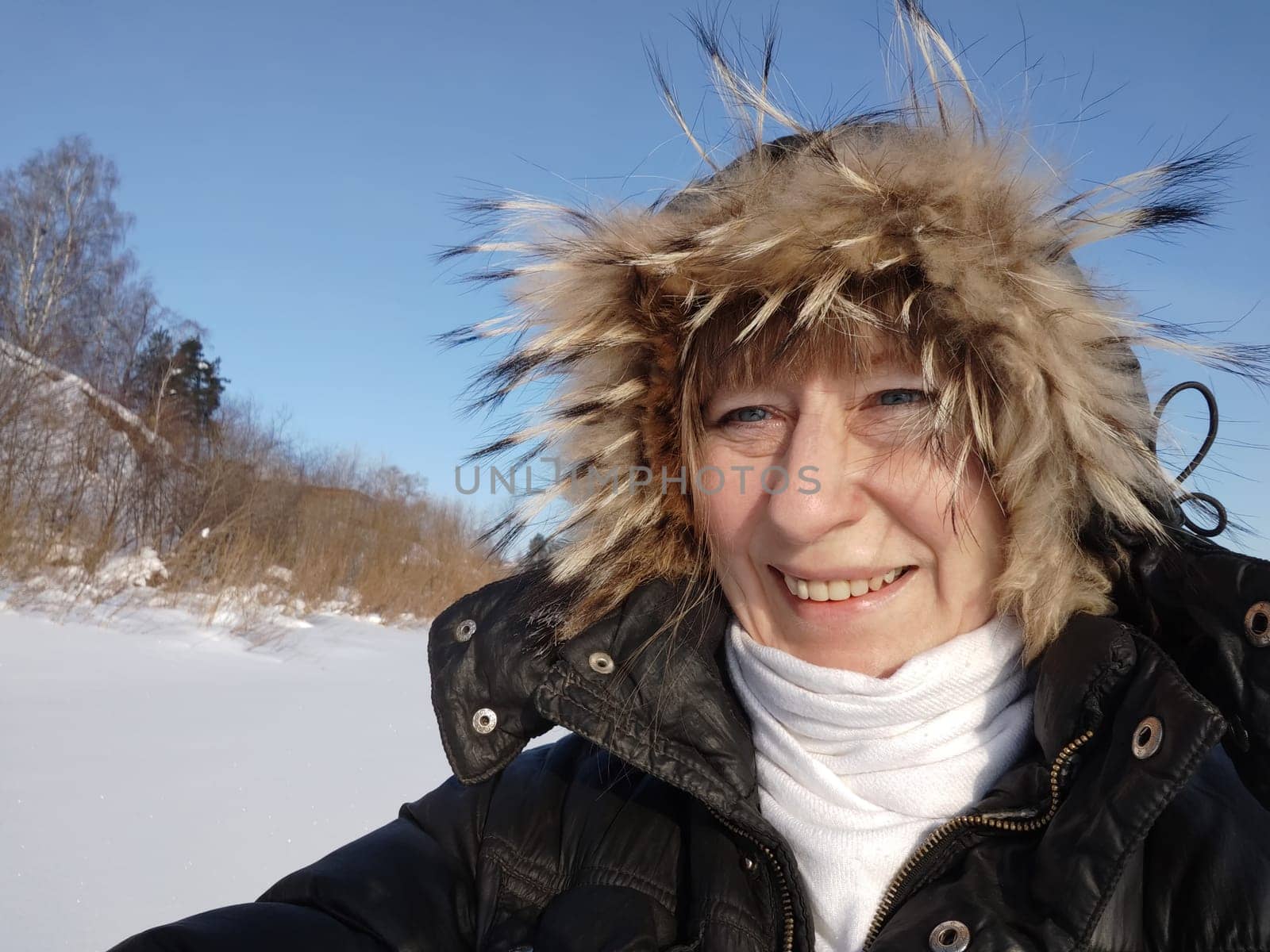 A cheerful girl or woman in a hooded jacket with fur on a sunny spring or winter day. An adult lady on cold day